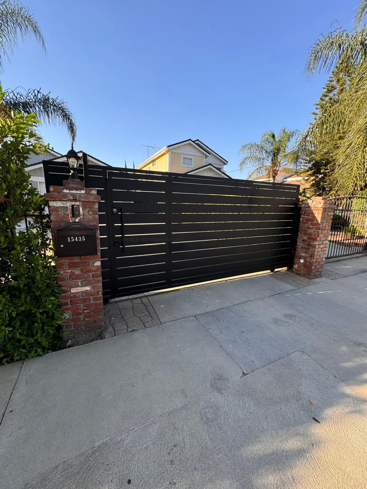Black slatted sliding gate between brick pillars