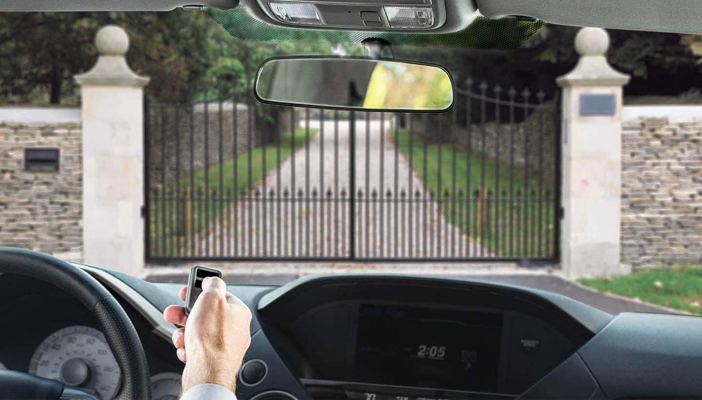 Driver using a gate remote at an iron driveway entrance